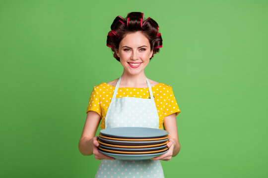 Photo of positive maid girl wash plates after family gathering hold pile stack wear yellow dotted dress hair rollers isolated over green color background