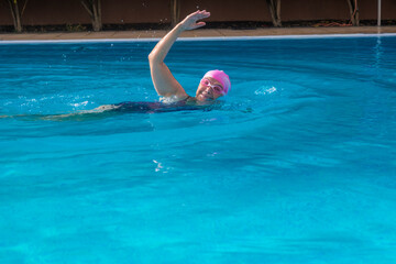 Senior woman swimming in outdoor swimming pool, smiling happy for healty activity wearing pink swimming cap and goggles