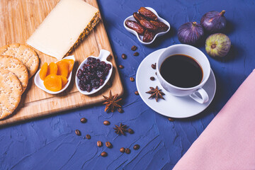 a cup of coffee, cheese, dried fruits, crackers, fresh figs, sprinkled coffee beans and a pink tablecloth