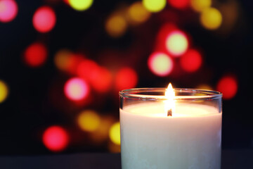 aroma scented ivory colour glass candle lighting on the black wooden table with the background of colourful bokeh lights in the dark restaurant during Christmas festival celebration event