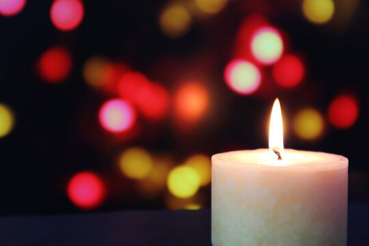 aroma scented ivory colour pillar candle lighting on the black wooden table with the background of colourful bokeh lights in the dark restaurant during Christmas festival celebration event
