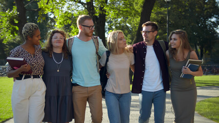 Happy university students walking together on campus chatting and laughing outdoors during break
