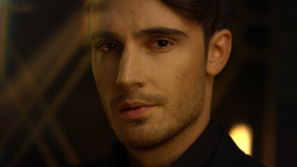 Doubt guy standing indoors. Attractive man gazing at camera in dark interior.