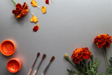 Bouquet of marigolds with brushes and orange paint on a gray background, top view, space for text
