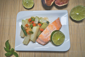 Gebratener Lachs mit Kohlrabi Gem&uuml;se, Karotten, Bohnen und einer Scheibe Limette auf einem wei&szlig;en Teller serviert