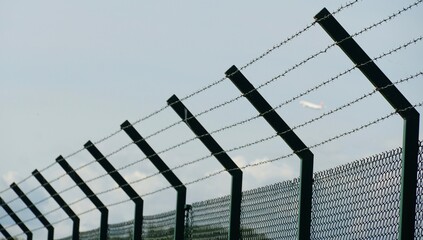 A tall fence around the ground of Zurich Airport made of woven wire and enhanced with barbed wire...