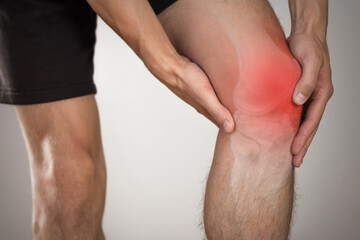 Pain in the knee of a man. Highlighted in red. On a gray background. Close up