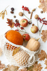 Eco friendly Thanksgiving, flat lay. Zero waste holidays, fall harvest. Reusable shopping bag with pumpkins, apples, berries, nuts and autumn leaves on white wooden background.