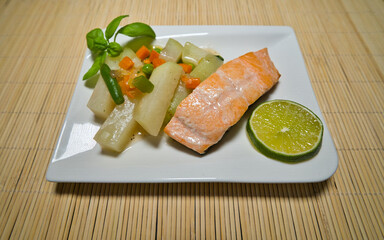 Gebratener Lachs mit Kohlrabi Gemüse, Karotten, Bohnen und einer Scheibe Limette auf einem weißen...