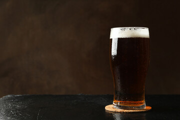 Glass of beer on black table against brown background