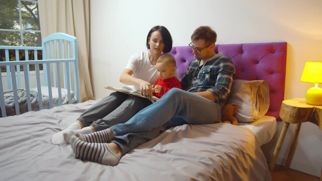 Mother, father and boy at home spending time together reading book in bed