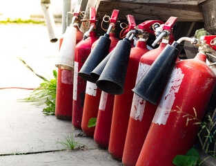 Several old red fire extinguishers stand in a row against the wall on the street. Fire...