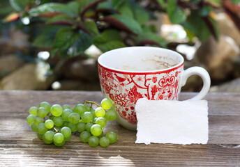 Breakfast in the garden, stationery mockup scene. A cup of coffee, blank business cards on a wooden bench.Grapes. Lifestyle concept, no people.