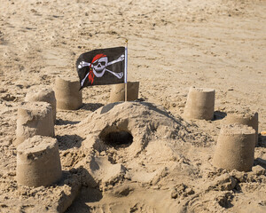 Tourism 2020, beach season. Children's figures built from sand are decorated with a pirate flag. Consequences Of Covin-19. Nobody. Beach season for travelers. Games with children on the sand by sea