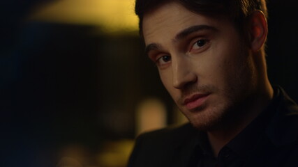 Obraz premium Charming guy raising eyebrows in dark background. Handsome man smiling indoors.
