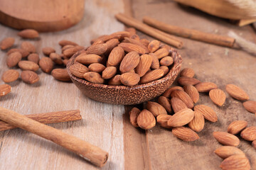 Almonds served on a small wood bowl with scattered almonds and cinnamons on the side
