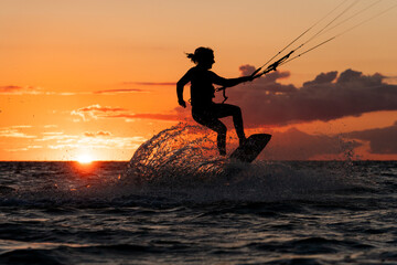 Silhouette of kitesurfer jumping with spray water in beautiful orange sunset conditions