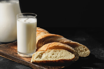 Glass of milk with sliced baguette on wooden board