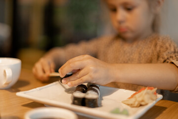 Cute little girl eating sushi in the cafe