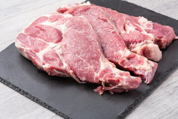 Several sliced steaks of pork neck on black stone board on gray kitchen table. Close up view.