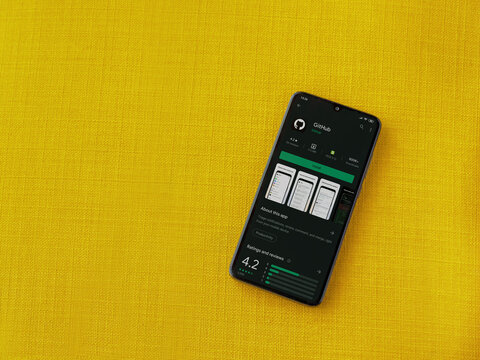 Lod, Israel - July 8, 2020: GitHub app play store page on the display of a black mobile smartphone on a yellow fabric background. Top view flat lay with copy space.