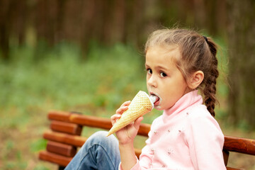 Cute little girl eating ice cream in the park while sitting on a bench