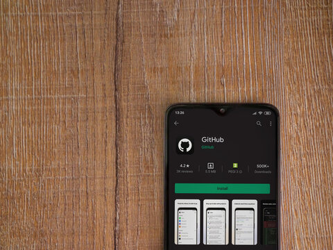 Lod, Israel - July 8, 2020: GitHub app play store page on the display of a black mobile smartphone on wooden background. Top view flat lay with copy space.