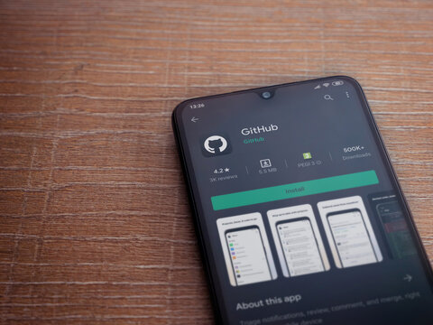 Lod, Israel - July 8, 2020: GitHub app play store page on the display of a black mobile smartphone on wooden background. Top view flat lay with copy space.