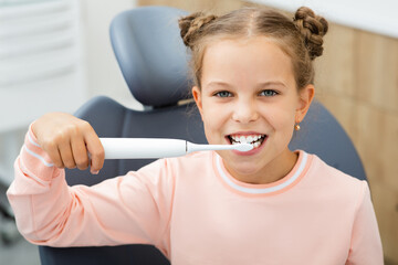 Pretty little girl cleaning teeth with electric sonic toothbrush. Perfect removing plaque with a modern toothbrush