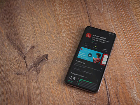 Lod, Israel - July 8, 2020: Adobe Acrobat Reader app play store page on the display of a black mobile smartphone on wooden background. Top view flat lay with copy space.