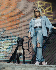 A girl is standing on the stairs with a pit bull on a leash. A girl and a fighting dog. girl in jeans and pitbull.