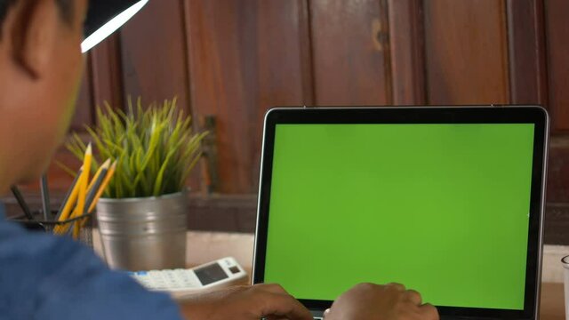 Over the shoulder shot of woman, using finger with keyboard for typing touch. computer laptop with blank green screen chroma key.