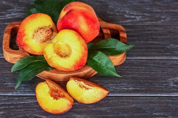 ripe peaches in a wooden bowl and green leaves close-up. background with whole peaches and half peaches
