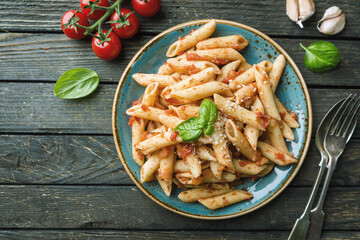 Penne pasta in tomato sauce and cheese decorated with basil on a wooden background, top view
