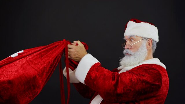Medium studio shot of shocked Santa Claus pulling Christmas sack trying to take gifts away from somebody against black background