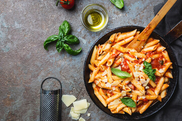 Penne pasta in tomato sauce and cheese decorated with basil on a gray stone background, top view