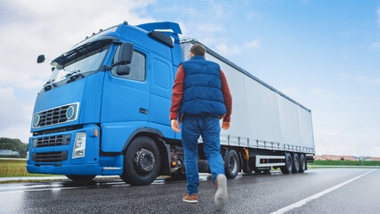 Truck Driver Crosses the Road in the Rural Area and Gets into His Blue Long Haul Semi-Truck with...