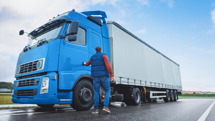 Truck Driver Crosses the Road in the Rural Area and Gets into His Blue Long Haul Semi-Truck with Cargo Trailer Attached. Logistics Company Moving Goods Across Countrie and Continent