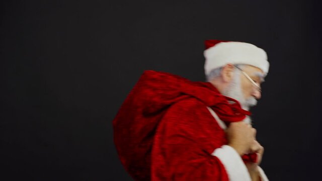 Medium studio shot of shocked Santa Claus pulling Christmas sack trying to take gifts away from somebody and finally walking away with presents