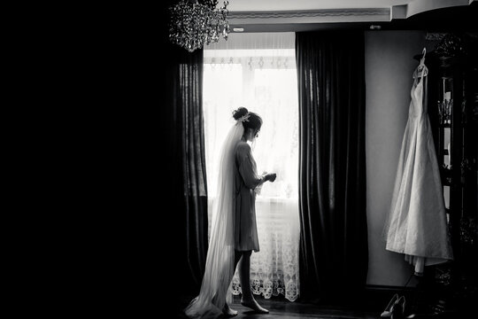 Black and white photo beautiful bride in a dressing gown poses near window