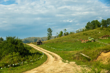 Fototapeta na wymiar Country road with a tractor in the mountains and on the horizon of high peaks