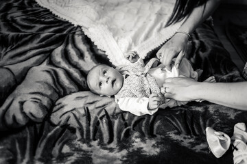 Black and white photo baby boy on a bed. Mother  dresses newborn child in suit for christening