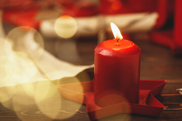 Burning Christmas red candle on brown wooden table