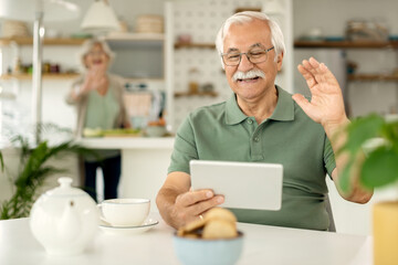 Fototapeta na wymiar Happy mature man having video call over touchpad and waving to someone.