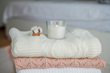 Fototapeta na wymiar A stack of knitted sweaters, cotton, a candle. Women's sweaters lie on the ottoman. Cozy autumn clothes.
