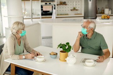 Fototapeta na wymiar Senior couple with face masks talking while sitting at the table at home.