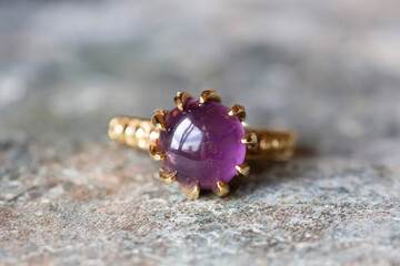 Brass metal decorative ring with natural mineral amethyst gemstone on grey neutral rocky background