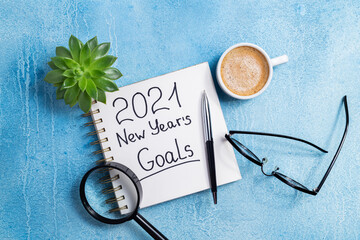 New year goals 2021 on desk. 2021 goals with notebook, coffee cup and eyeglasses on blue...