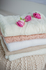 Fototapeta na wymiar A stack of knitted sweaters, roses. Women's sweaters lie on the ottoman. Cozy autumn clothes.