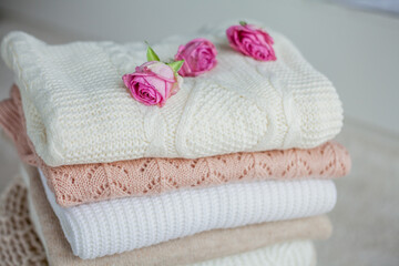 Obraz na płótnie Canvas A stack of knitted sweaters, roses. Women's sweaters lie on the ottoman. Cozy autumn clothes.